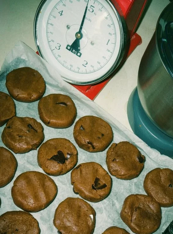 Des pâtons de cookies sur papier cuisson, à côté d'une balance de cuisine rouge