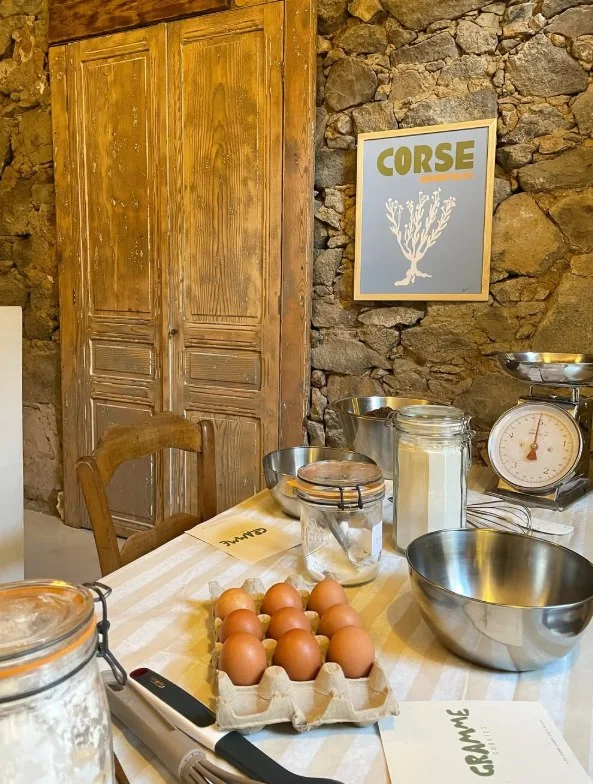 La boutique : murs de pierre, porte ancienne, affiche « Corse » et table de préparation